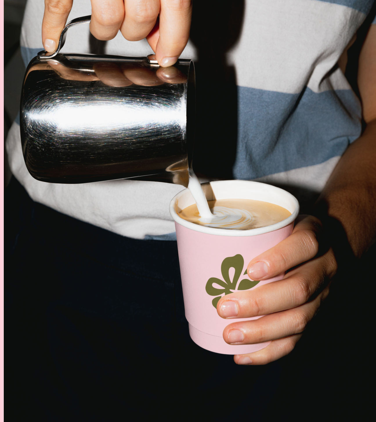 Barista sirviendo leche sobre un latte en vaso rosa